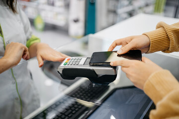 Detail of a client hands paying with the smartphone at a pharmacy
