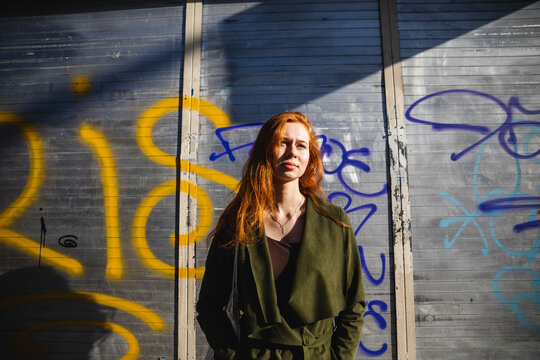 Woman with red hair standing in the sun with shutter on the background