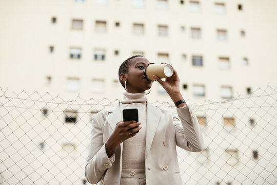 Black woman with smartphone drinking on street