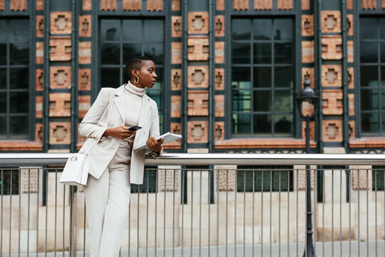 Black businesswoman with smartphone leaning on fence