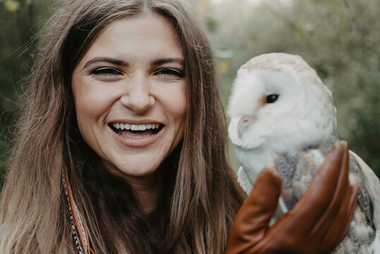 A woman in her twenties posing for a portrait with an owl in a forest