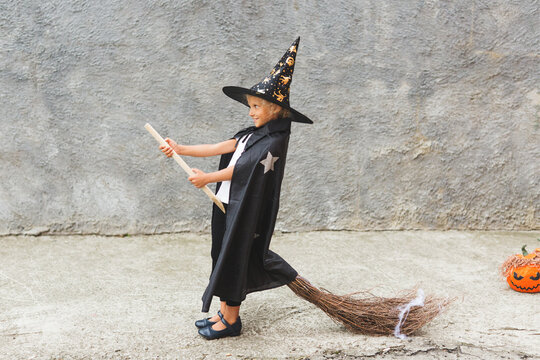 Girl in Halloween costume having fun. A little girl in a witch costume is playing outdoor. Little girl witch costume with a broom