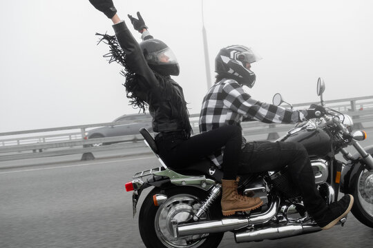 Attractive couple riding vintage motorcycle across the bridge over river, foggy weather.