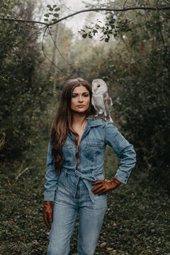 A woman in her twenties posing for a portrait with an owl in a forest