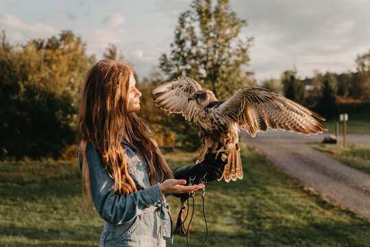 A woman in her twenties posing for a portrait with an owl in a forest