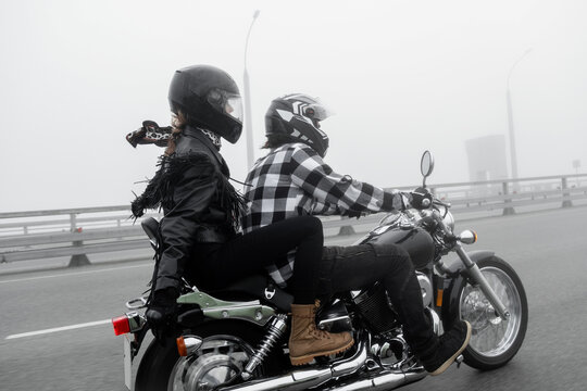 Attractive couple riding vintage motorcycle across the bridge over river, foggy weather.