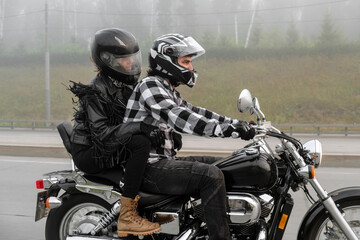 Attractive couple riding vintage motorcycle across the bridge over river, foggy weather.