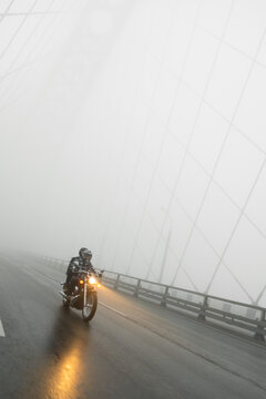 Attractive couple riding vintage motorcycle across the bridge over river, foggy weather.