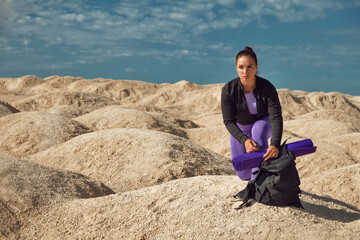 woman with backpack sitting on one knee on yellow dunes looks into distance on sunny day