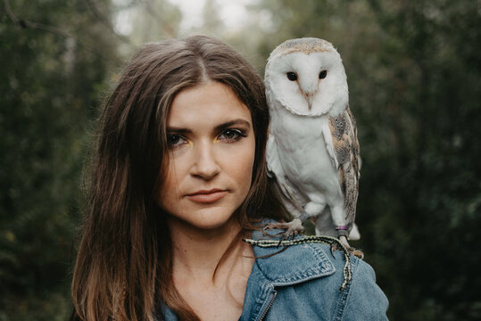 A woman in her twenties posing for a portrait with an owl in a forest