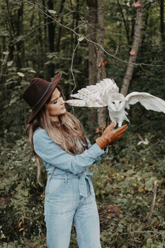 A woman in her twenties posing for a portrait with an owl in a forest