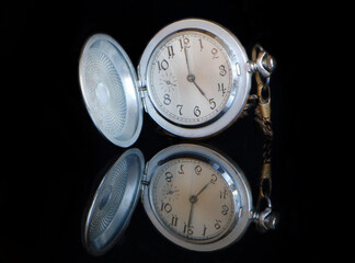 Antique silver watch with frayed dial on a contrasting black background with reflection in glass