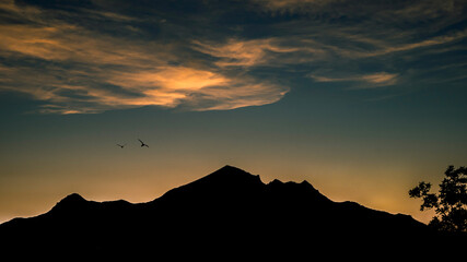 Silhouette of the mountain at sunset and flying birds in the beautiful sky.