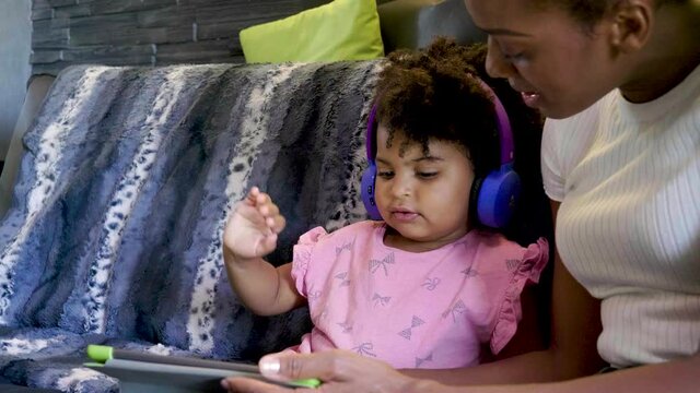 Mother and daughter using tablet and listening to music on sofa
