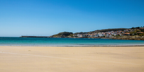 wide beach with fine sand and the calm blue sea in the background and the town of corme. Ermida Beach