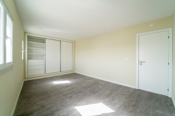 Empty room with dark wooden floating laminate flooring and wardrobe. House interior, wide bedroom space. Newly recently painted new apartment or house. Wood floor. Real state and property management