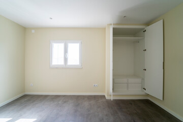 Empty room with dark wooden floating laminate flooring and wardrobe. House interior, wide bedroom space. Newly recently painted new apartment or house. Wood floor. Real state and property management