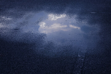 Puddle of water on asphalt road reflecting the sky,dramatic scene after hard rain fall.