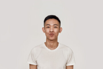 Kiss. Portrait of young asian man with clean shaven face looking playful while blowing, giving a kiss at camera isolated over white background. Beauty, skincare, facial expression