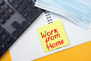 Computer keyboard, face mask, notepad and sticky notes on the yellow background with Work from home text