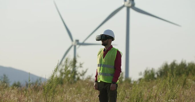 Engineer in VR glasses looking at graphs, turning pages. Windmills in the background