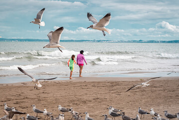 mom and daughter on vacation walking on the beach with seagulls in the background