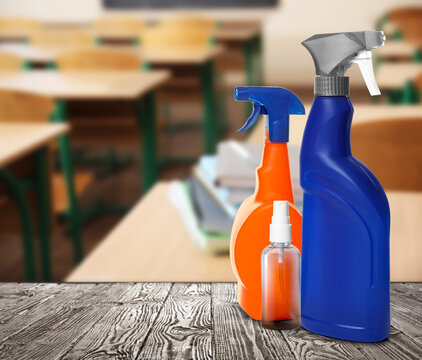 Protective measures during Coronavirus pandemic. Bottles of disinfectant and hand sanitizer on table against classroom, space for text