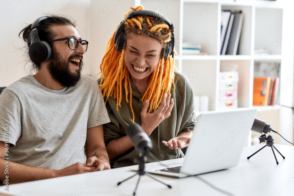 Wall mural laughing together. couple of bloggers, young man and woman in headphones watching something on lapto