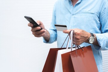 Midsection of man holding shopping bags using mobile phone and credit card