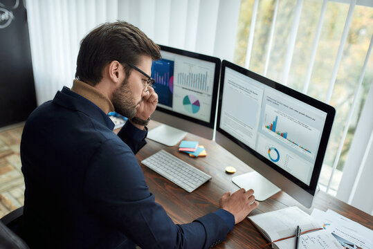 Focused successful businessman or financial analyst working in the modern office, looking at graphs and charts on pc screen and analyzing statistical data