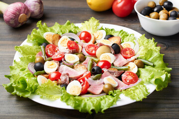 A large platter of tuna salad (nicoise) stands on a wooden table.