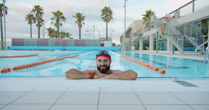 Happy muscular athlete smiling after his morning training in olympic swimming pool. Slow motion 4k video