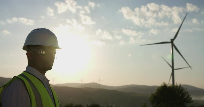 The engineer, looking at the windmill, turns his head to the camera. Sunset