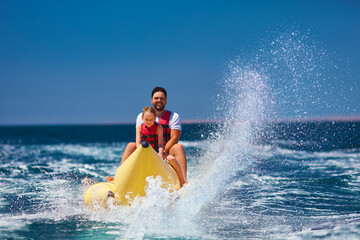 happy family, delighted father and son having fun, riding on banana boat during summer vacation