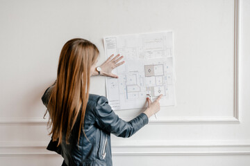 Red haired female engineer painting by pencil on map.