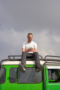 Man visiting Bromo volcano by jeep and sitting on the top of the car using a mobile phone