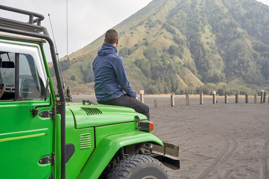 Man visiting Bromo volcano by jeep and sitting on the hood of the car