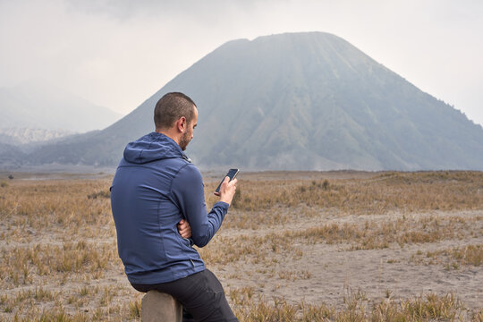 Man visiting Bromo volcano by jeep and using a mobile phone