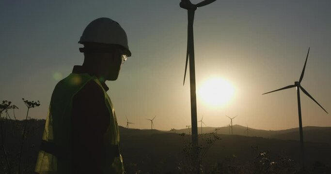A young engineer inspects the windmills, hiding his hand from the sun