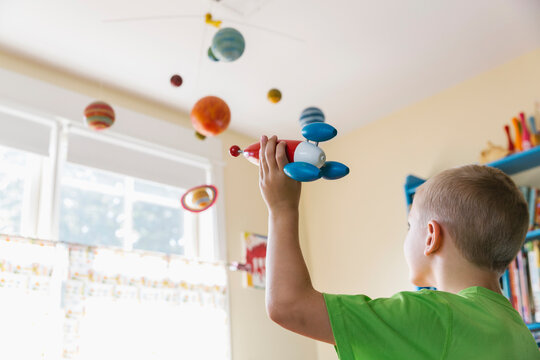 Child in Bedroom Playing Astronaut with Toy Rocket Ship and Solar System Mobile