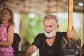 senior handsome elderly caucasian old man having fun with carousel  in the park outdoors, senior...