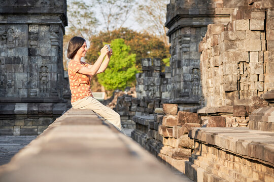 Woman using cell phone to take pictures in Prambanan Temple, Java, Indonesia