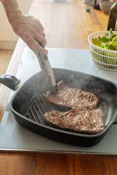 Faceless woman frying juicy steaks for meal