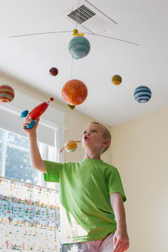 Child having fun Playing Astronaut with Toy Rocket Ship and Solar System Mobile