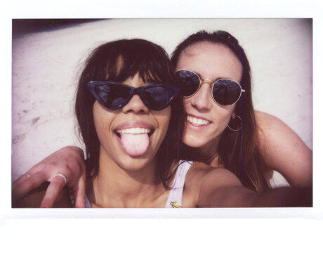 Two girlfriends showing tongue, resting on beach.