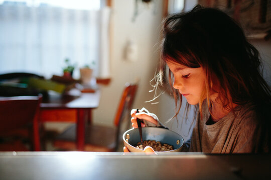 little girl eats cereal for breakfast in morning sun