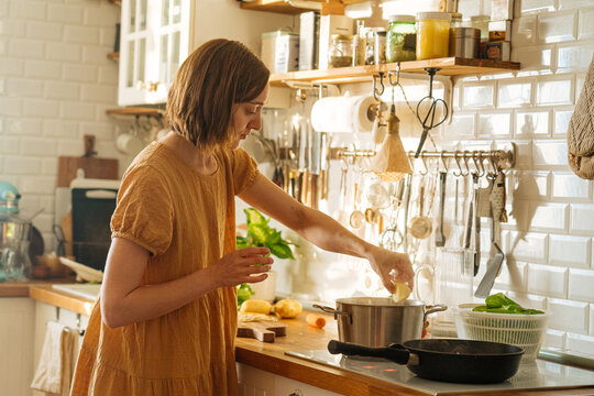 Young woman cooking soup in kitchen