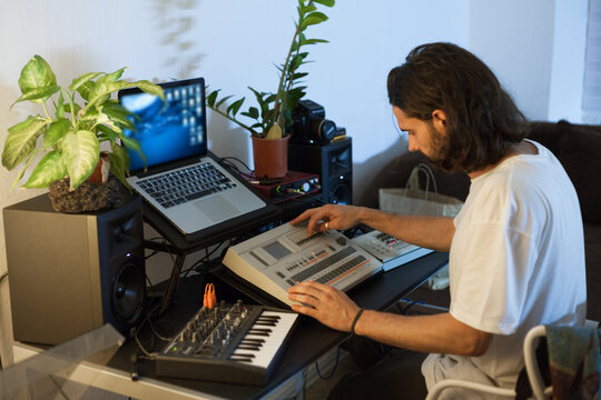 copywriter in a white T-shirt with long hair writes music on electronic instruments while sitting