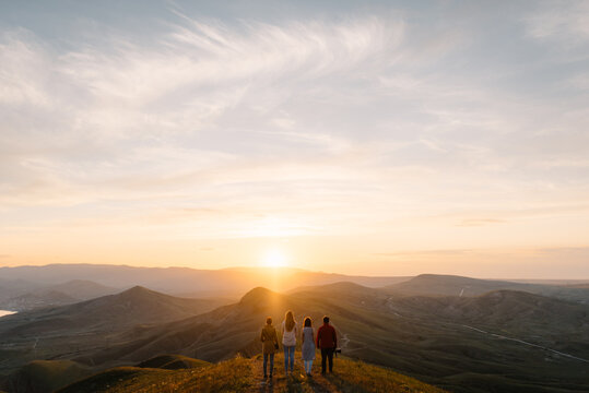 group of people stands in mountains and watches how the sun sets