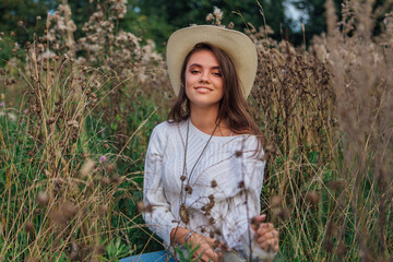 Young beautiful brunette woman sitting on the grass, smiling and touching her hair